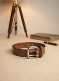 Brown leather belt with silver buckle on a beige surface with a blurred background