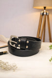 Black leather belt with silver buckle on a light surface, with a lamp in the background.